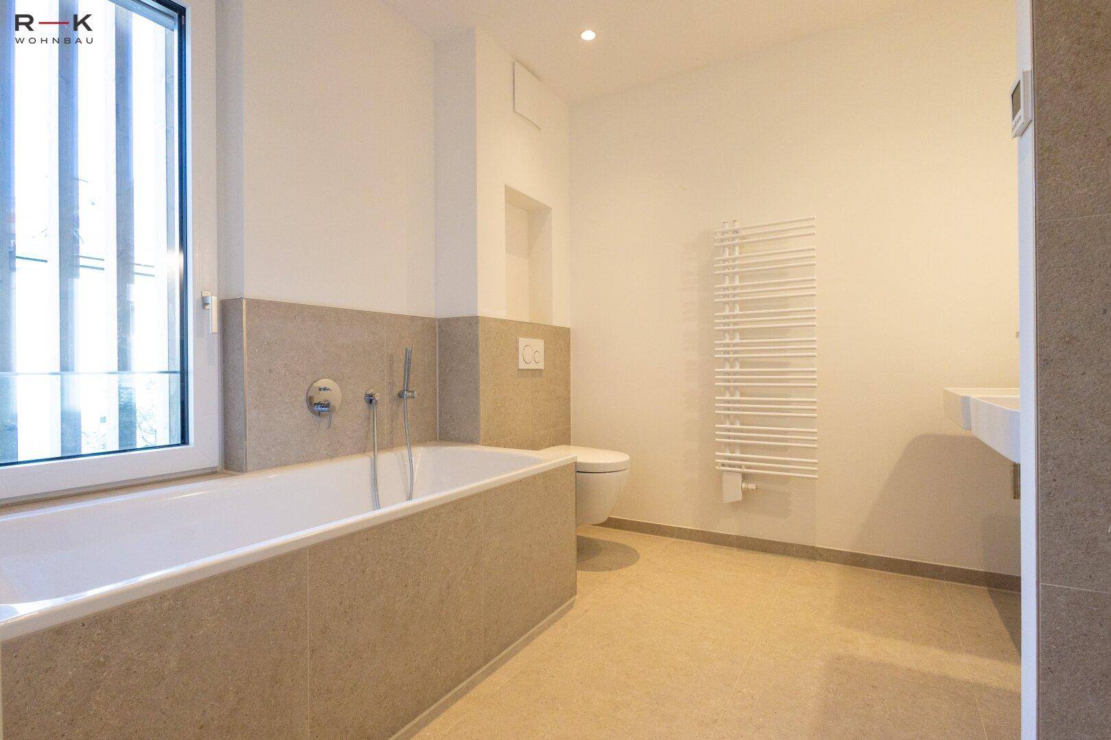 Helles Badezimmer mit Badewanne, wandhängendem WC und beheiztem Handtuchhalter.