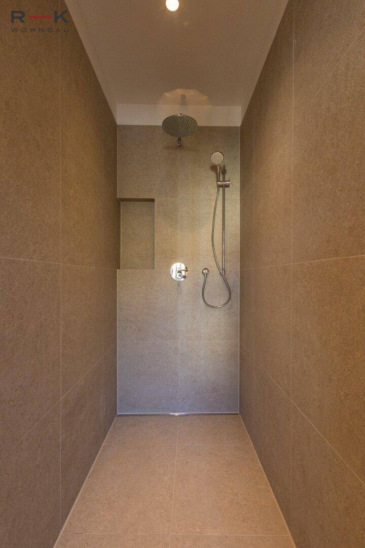 Ebenerdige Dusche mit Regenduschkopf und modernen Fliesen in einem minimalistischen Badezimmer.