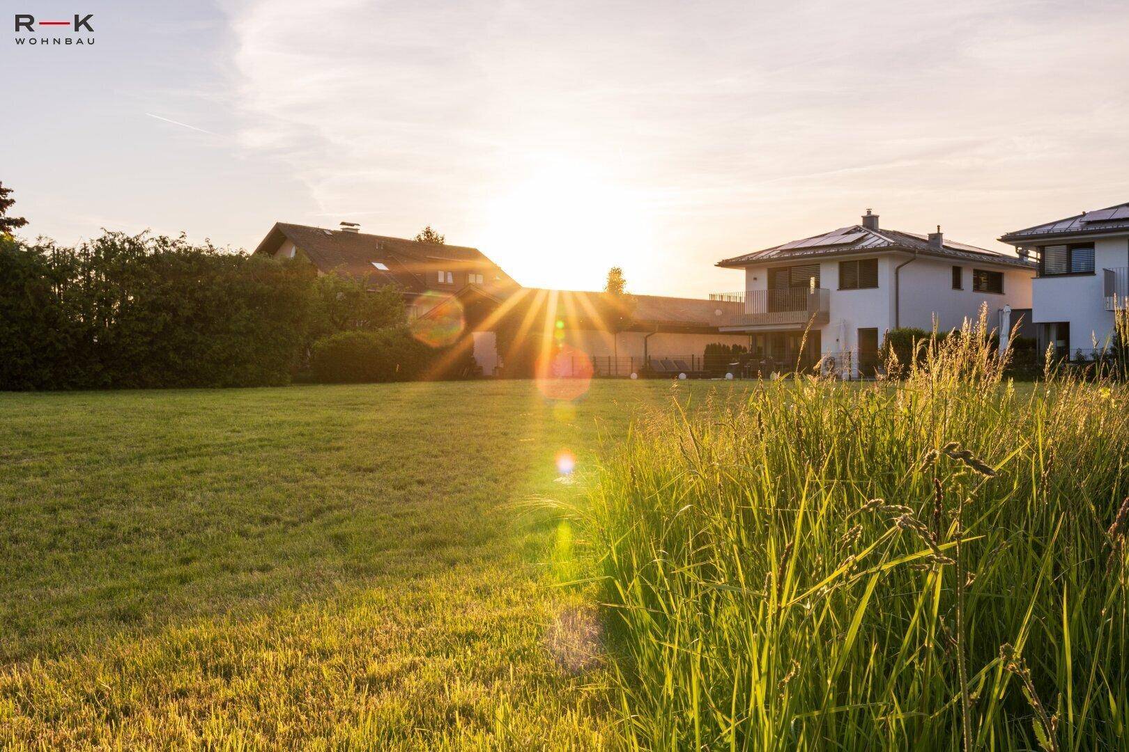 Sonnenuntergang über einem weitläufigen Rasenbereich mit Wohnhäusern im Hintergrund.