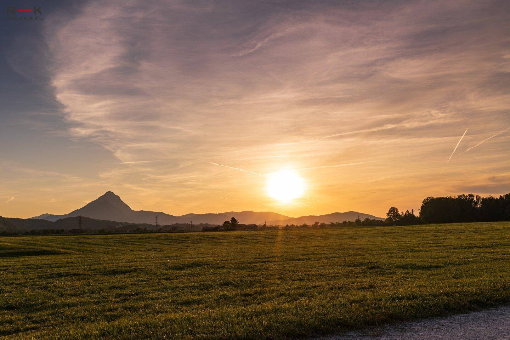 Spektakulärer Sonnenuntergang über einer weiten Wiesenlandschaft mit Bergen am Horizont.