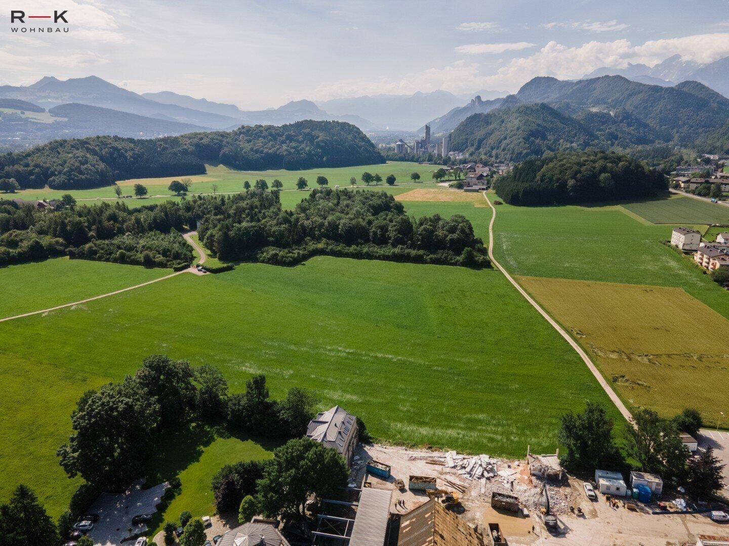 Weitläufige Luftaufnahme mit grünen Feldern, Wäldern, einer Stadt in der Ferne und Bergen am Horizont.