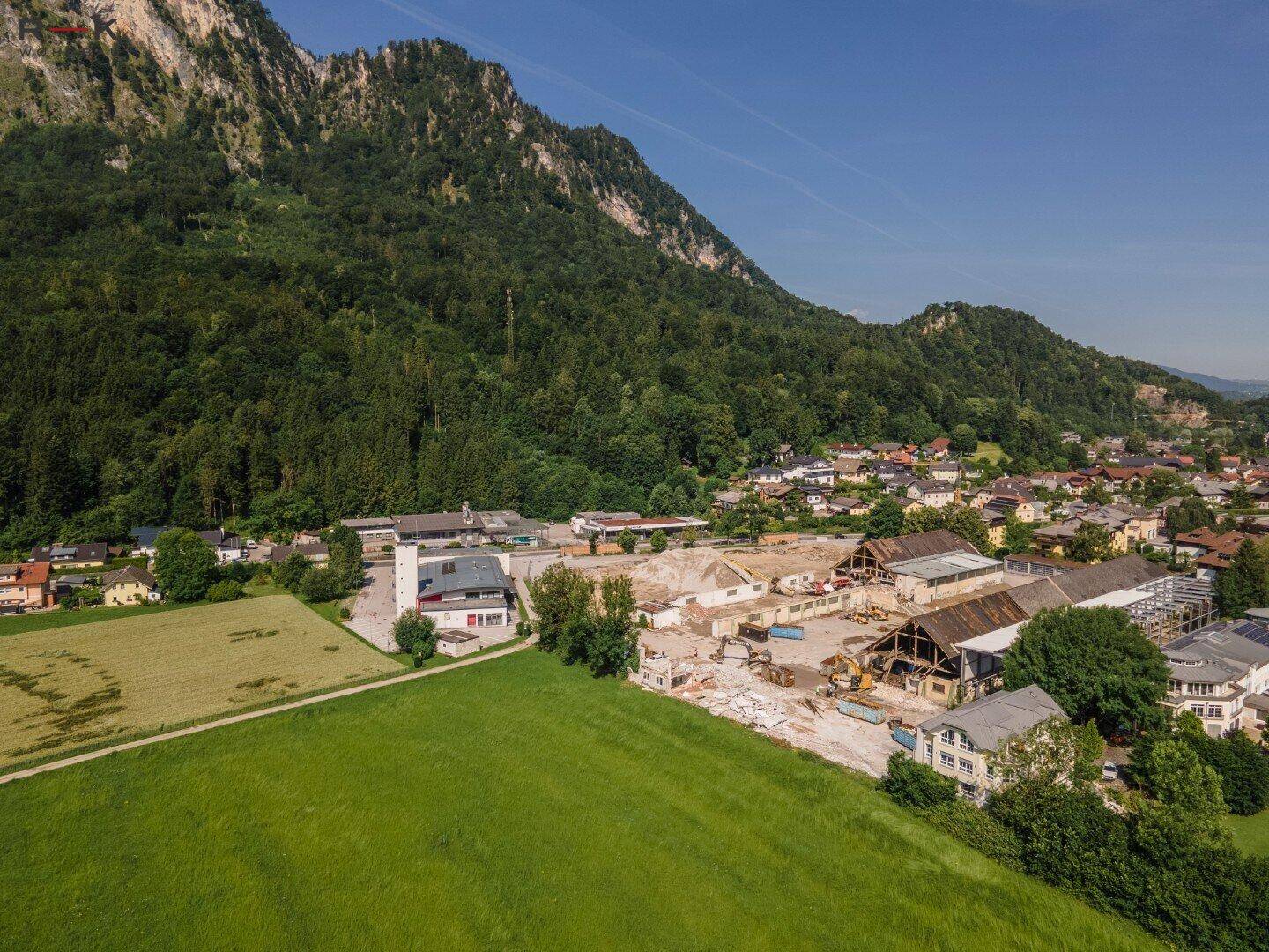 Luftaufnahme einer Stadt am Fuße eines Berges mit einer Baustelle im Zentrum der Ansicht.
