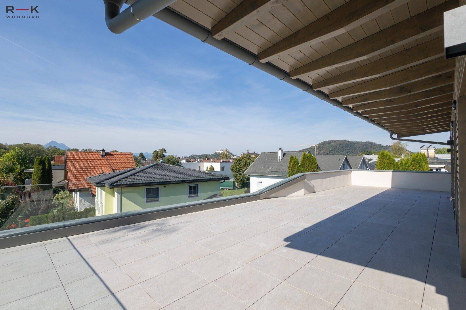 Große, geflieste Dachterrasse mit Glasgeländer und weitem Blick über die Umgebung.