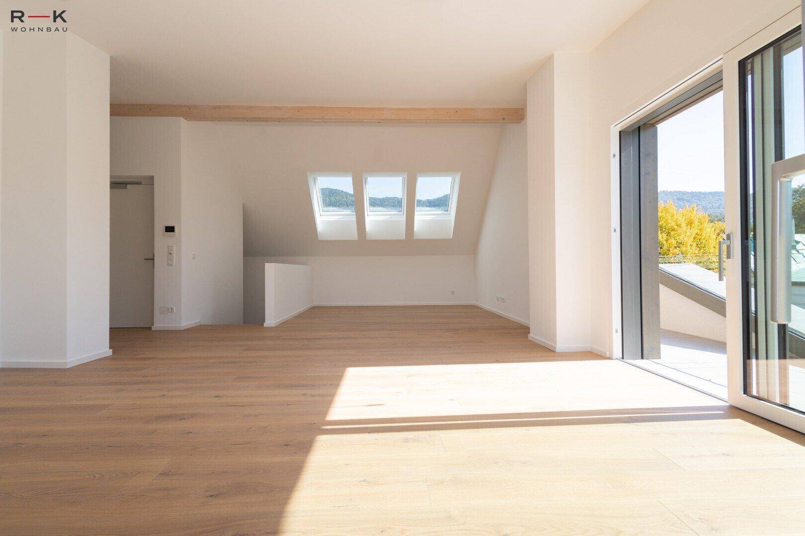 Heller Dachgeschossraum mit Holzbalken, Dachfenstern und Zugang zu einem Balkon.