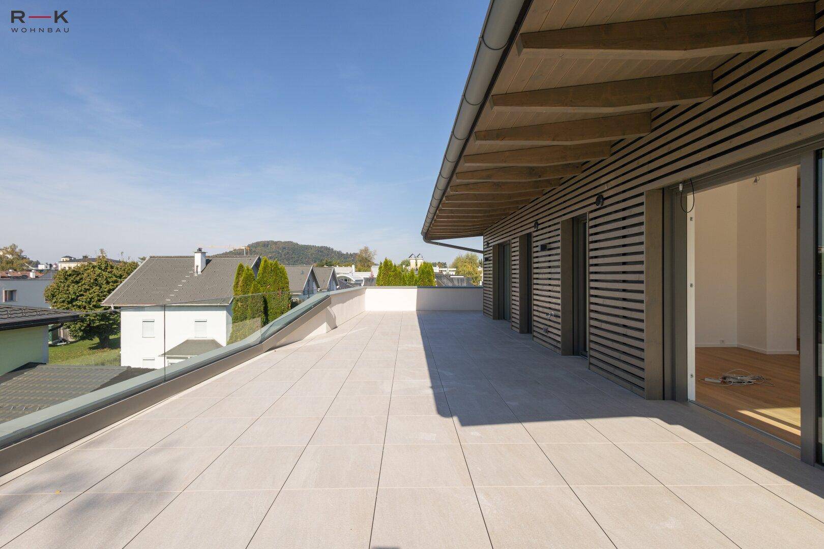 Moderne Dachterrasse mit Holzfassade und großen Schiebetüren, die den Zugang zum Innenbereich ermöglichen.