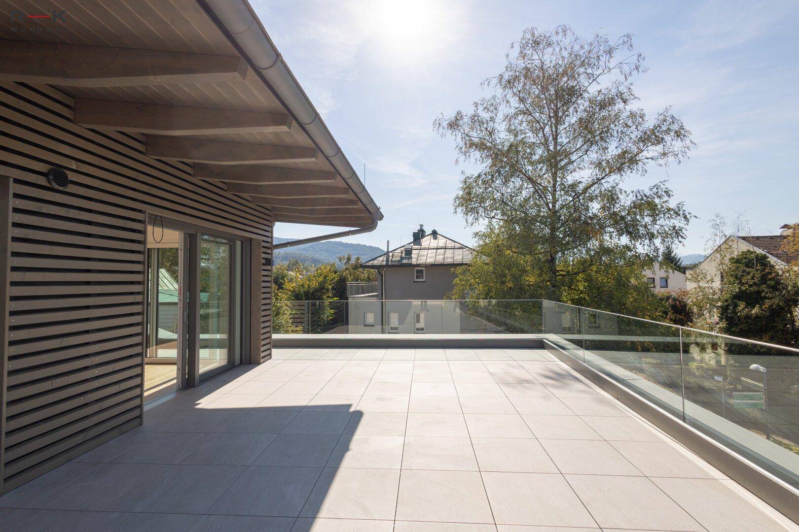 Sonnige Dachterrasse mit Holzverkleidung und raumhohen Fenstern, die einen hellen Außenbereich schafft.