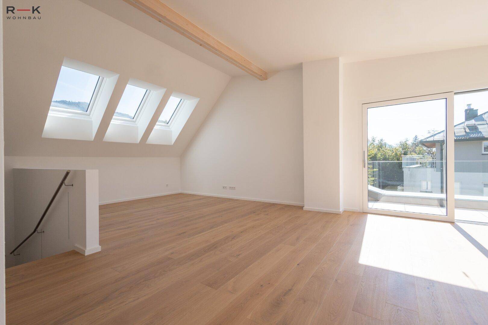 Geräumiger Dachgeschossraum mit Holzboden, Dachfenstern und Zugang zu einer Außenterrasse.
