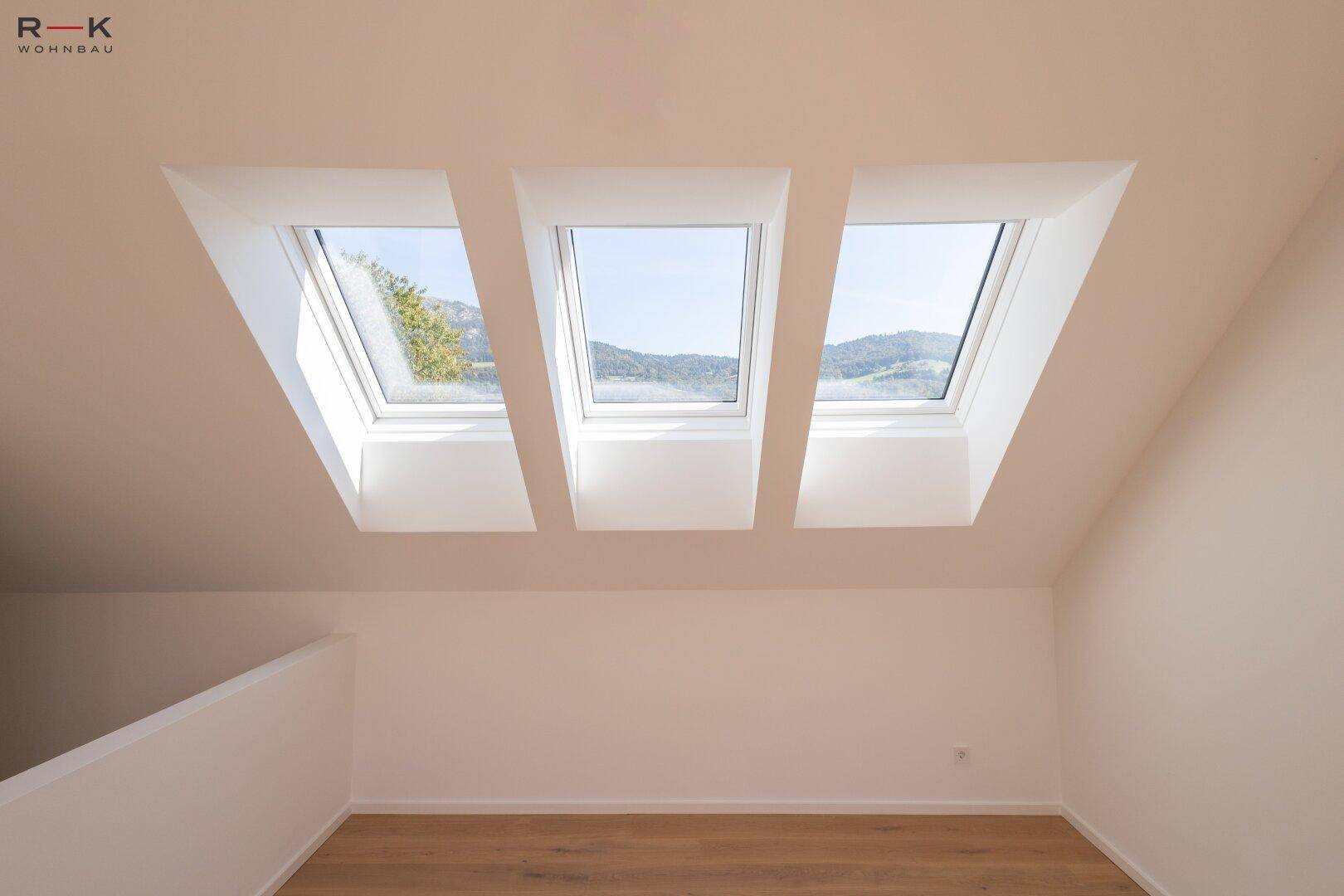 Drei große Dachfenster in einer schrägen Decke, die den Raum mit natürlichem Licht durchfluten.