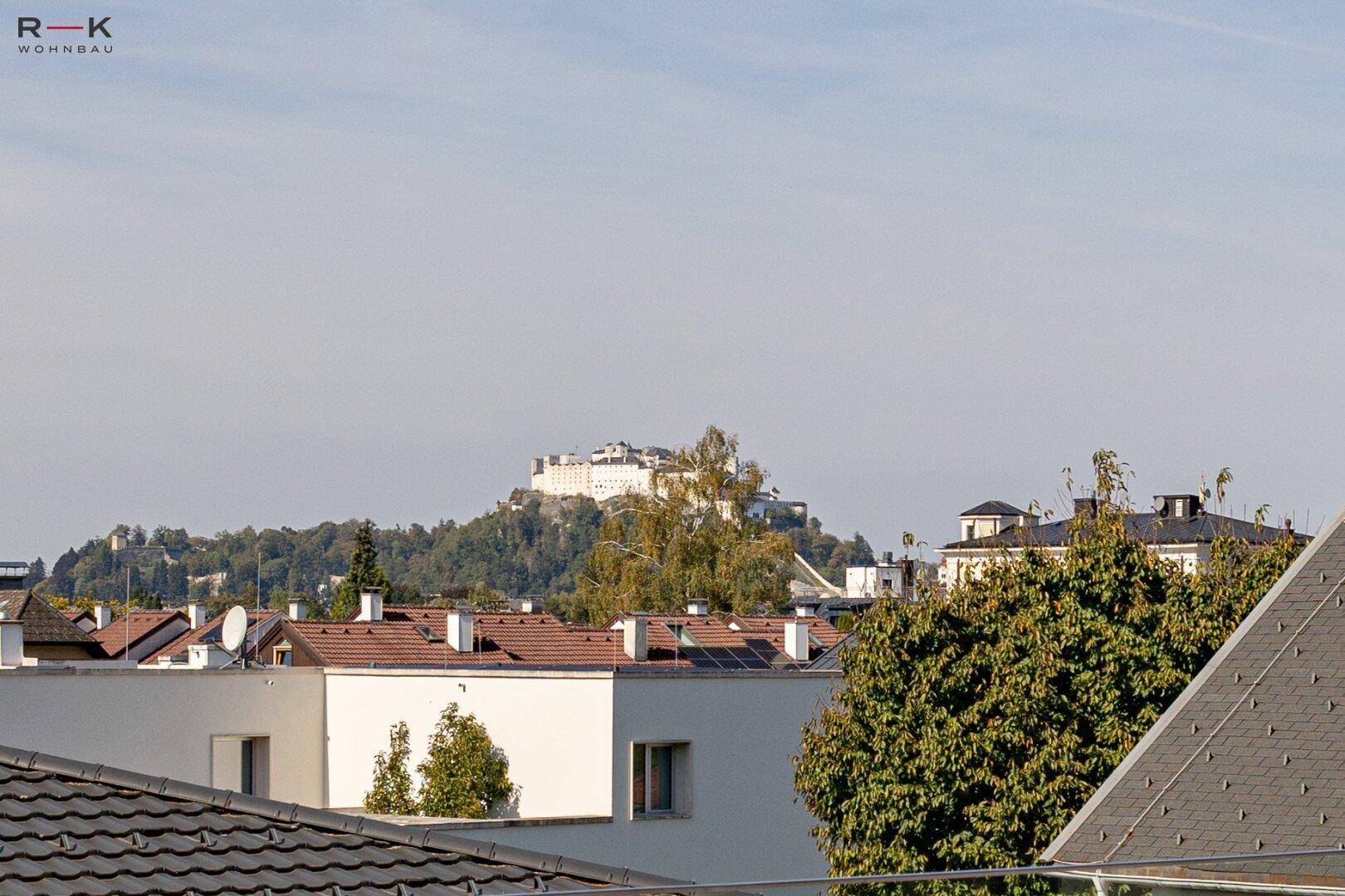 Panoramablick über die Dächer der Stadt mit einer historischen Festung auf einem Hügel im Hintergrund.