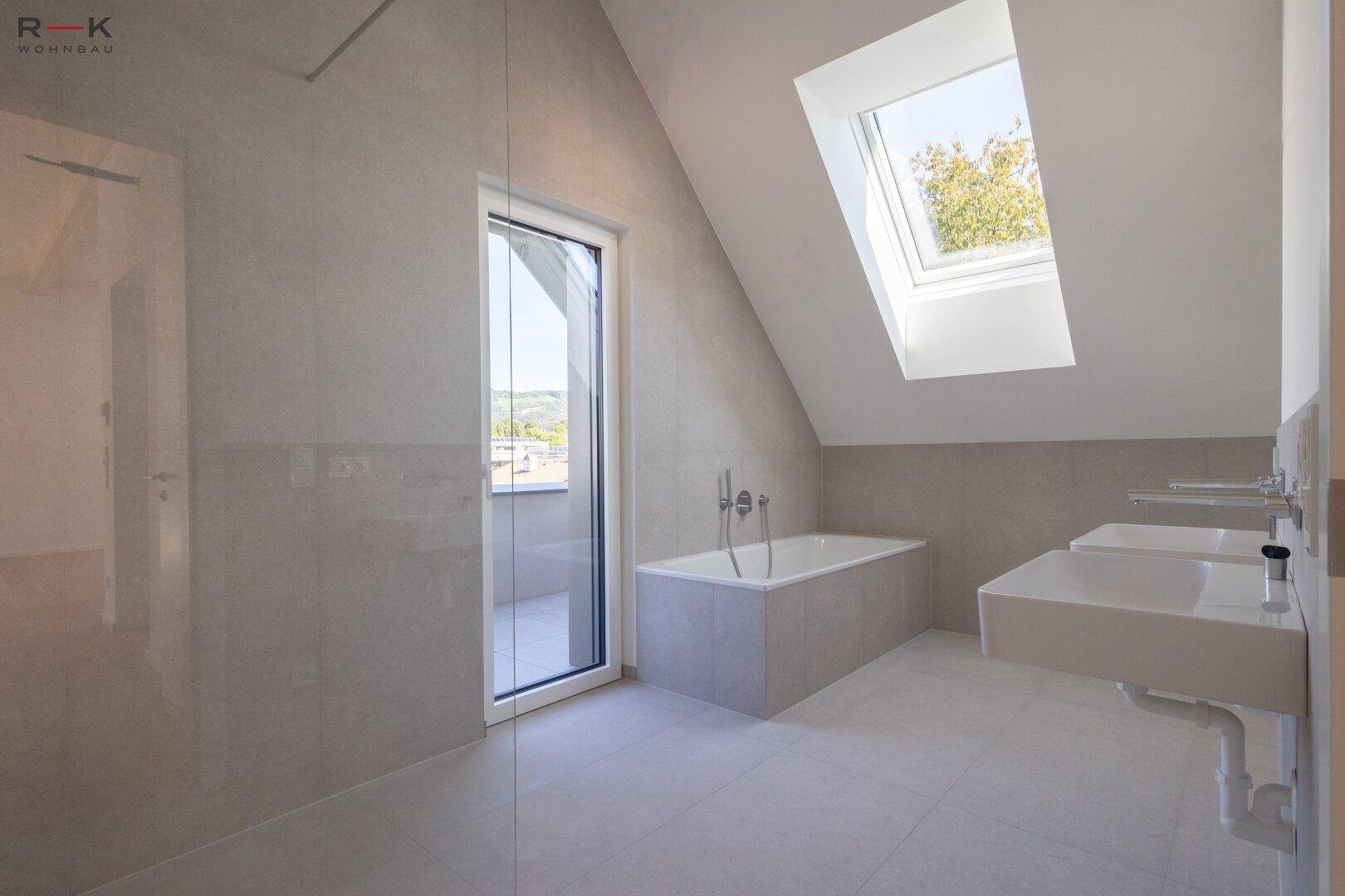 Modernes Badezimmer mit grauen Fliesen, Badewanne, Doppelwaschbecken und Dachfenster für viel Licht.