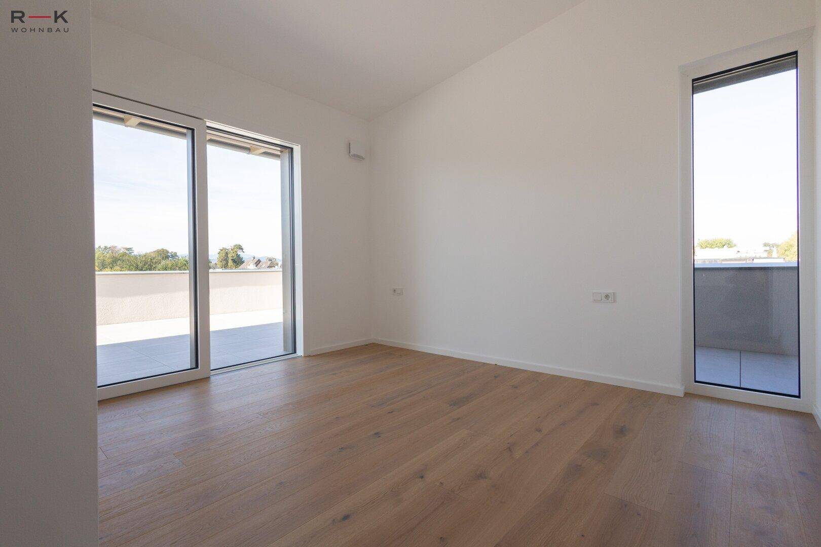 Helles Zimmer mit Holzboden und Zugang zu einer Terrasse sowie einem französischen Balkon.