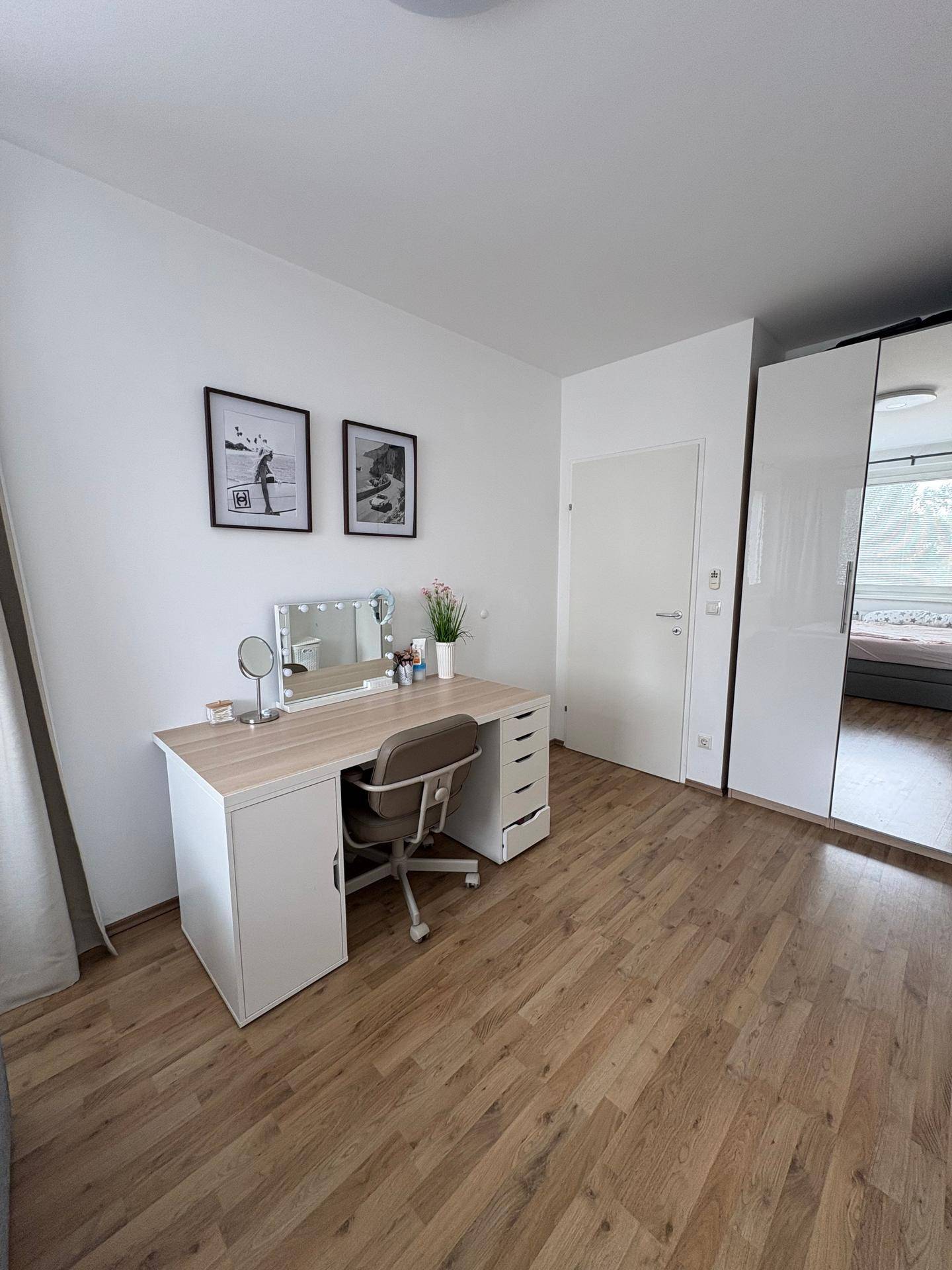 Schlafzimmer mit Schreibtisch, Spiegelschrank und hellem Holzboden.