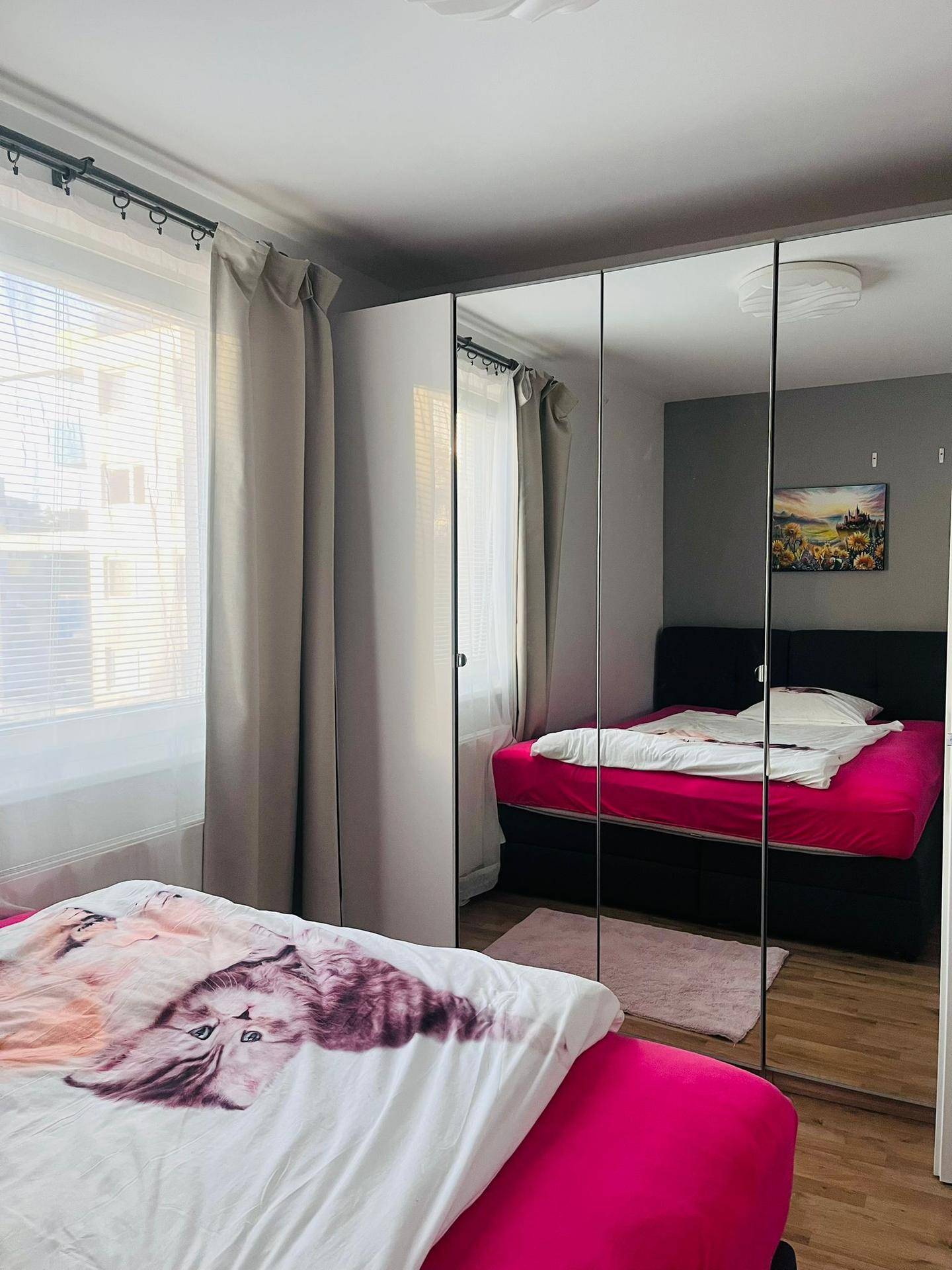 Schlafzimmer mit großem Spiegelschrank, Doppelbett und hellem Fenster.