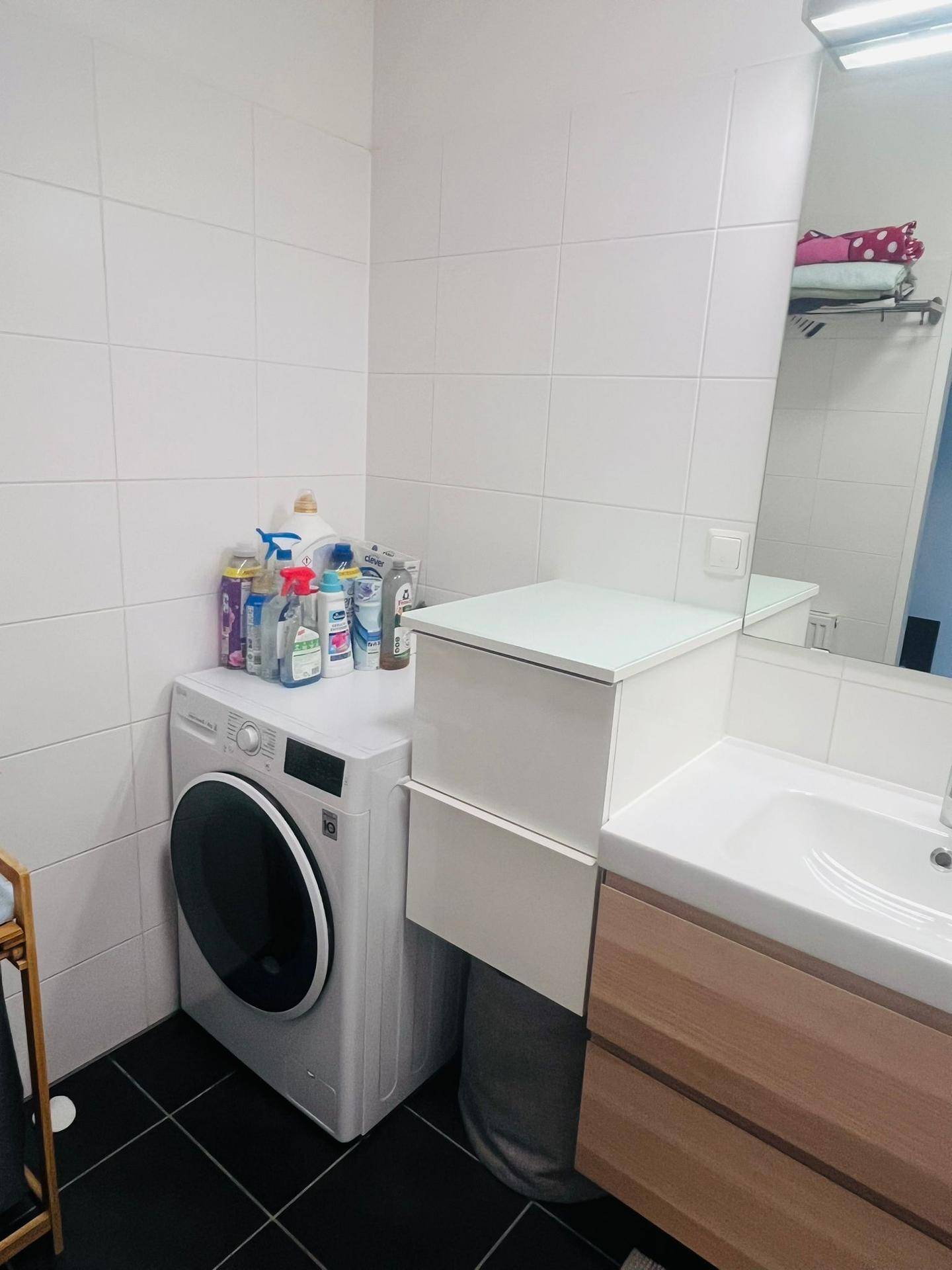 Badezimmer mit Waschmaschine, Waschbecken und weißen Wandfliesen.