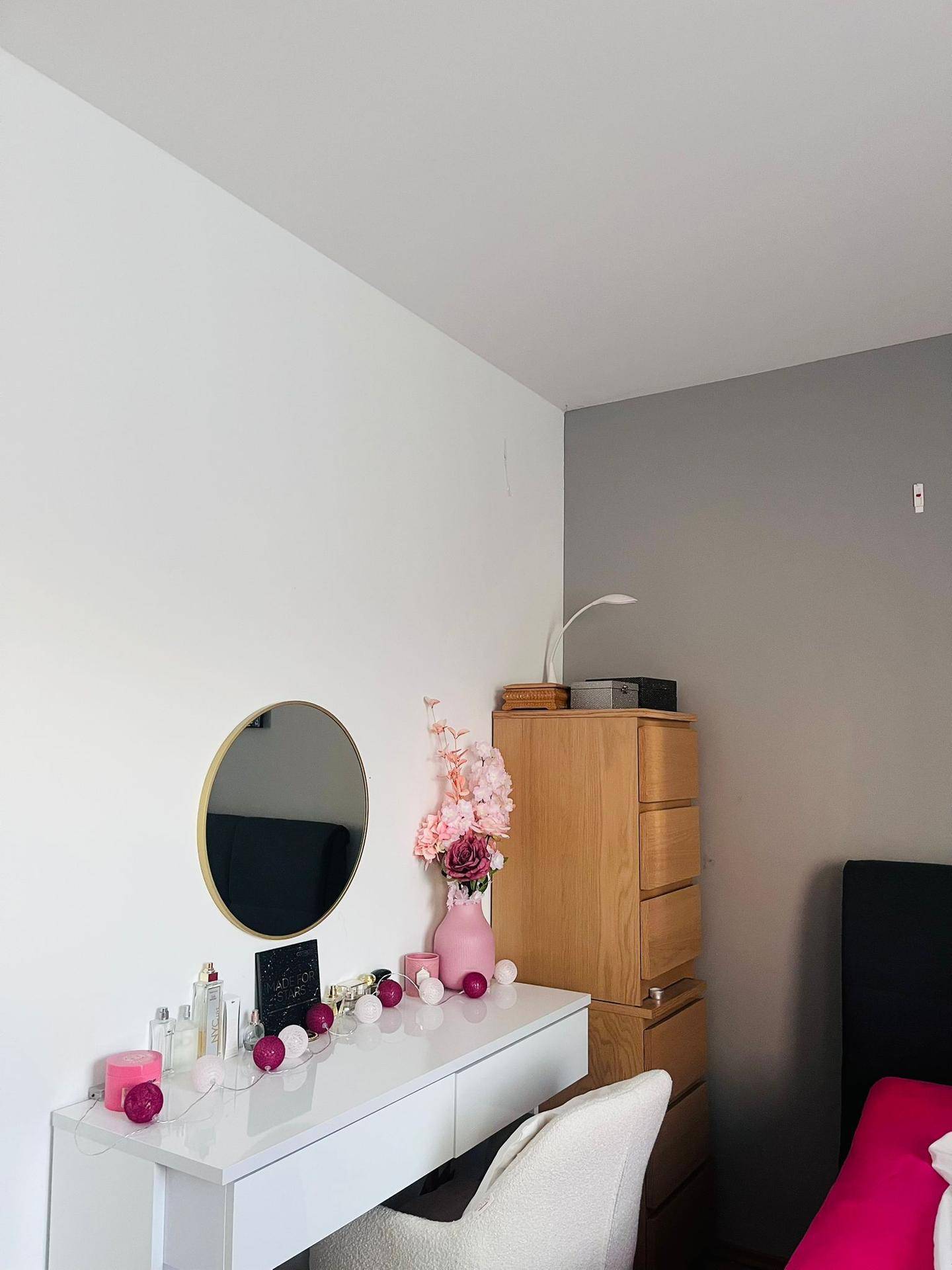 Schminktisch mit rundem Spiegel und pinker Dekoration in einem hellen Schlafzimmer.