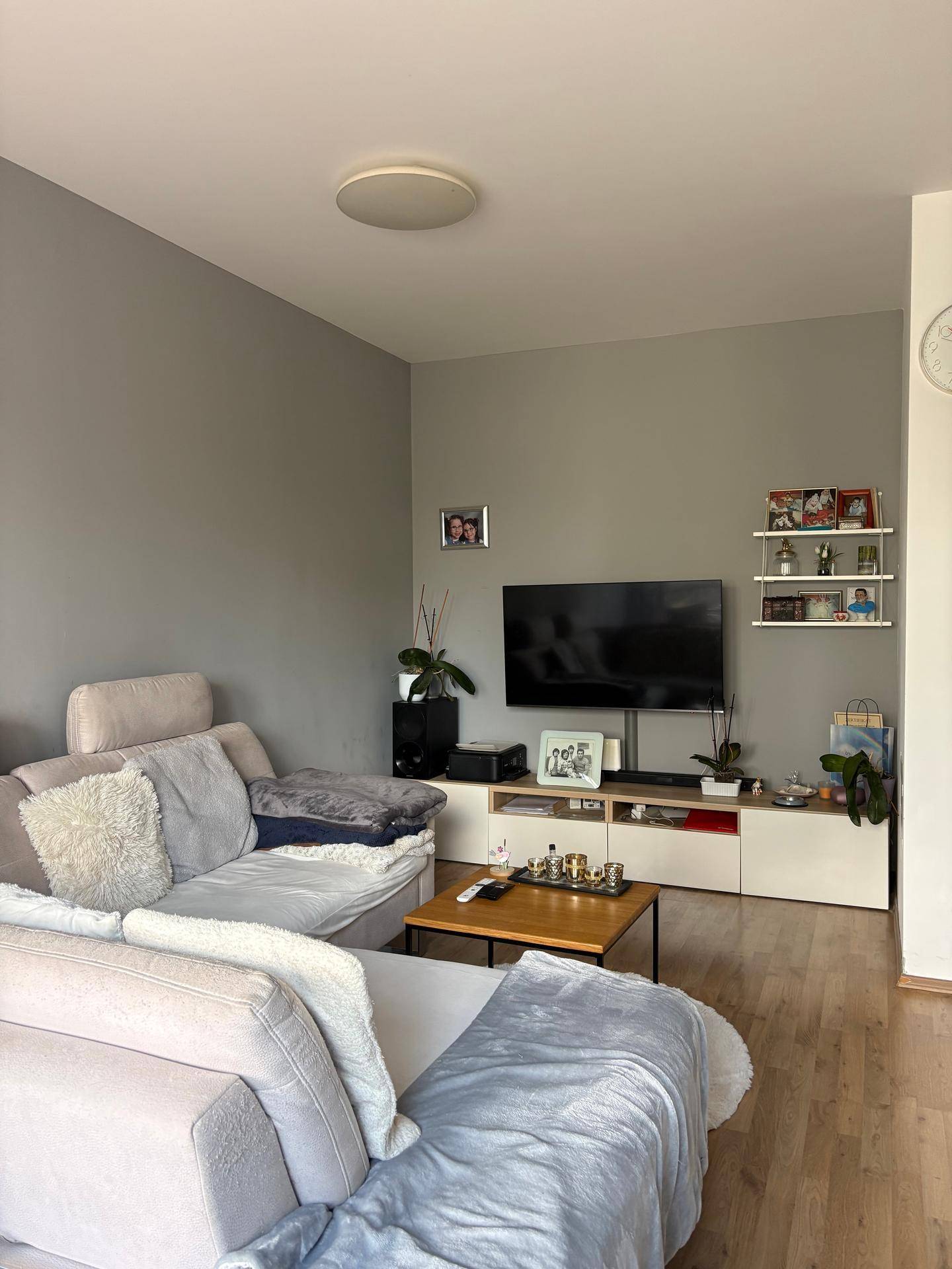 Gemütliches Wohnzimmer mit grauem Ecksofa, Holzboden und modernem TV-Möbel.