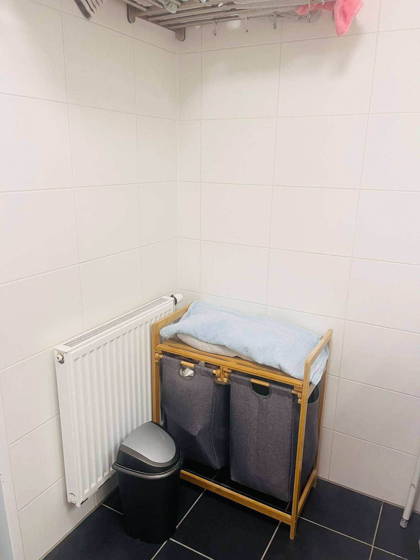 Badezimmer mit Heizkörper und Wäschekörben, komplett mit weißen Fliesen.