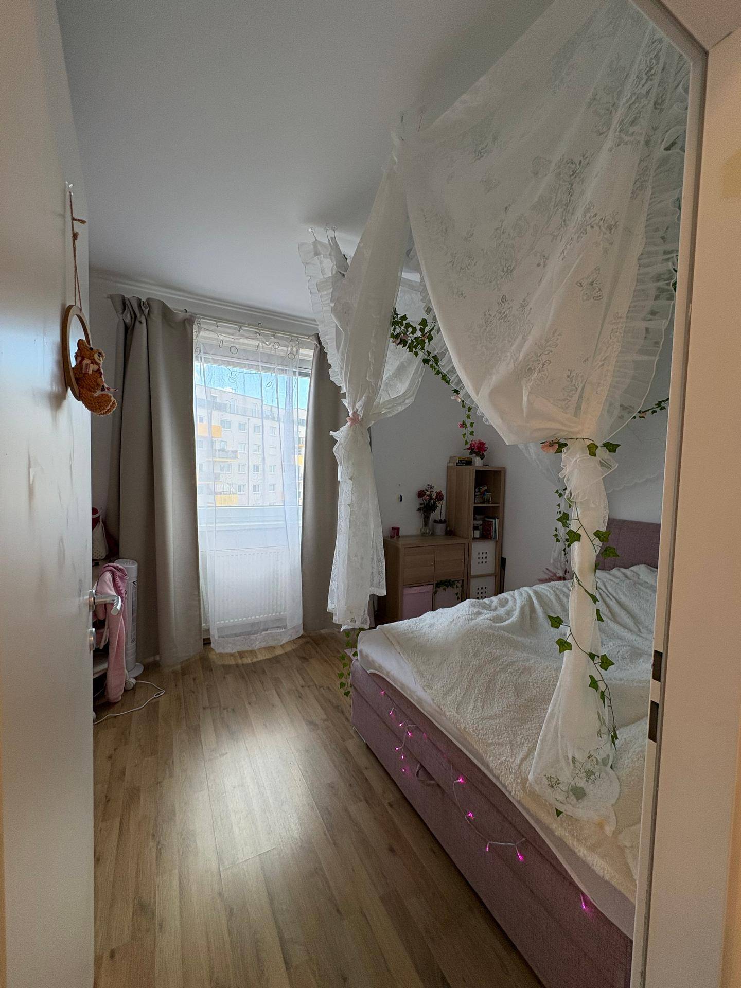 Helles Schlafzimmer mit Himmelbett, großem Fenster und Vorhängen für Privatsphäre.