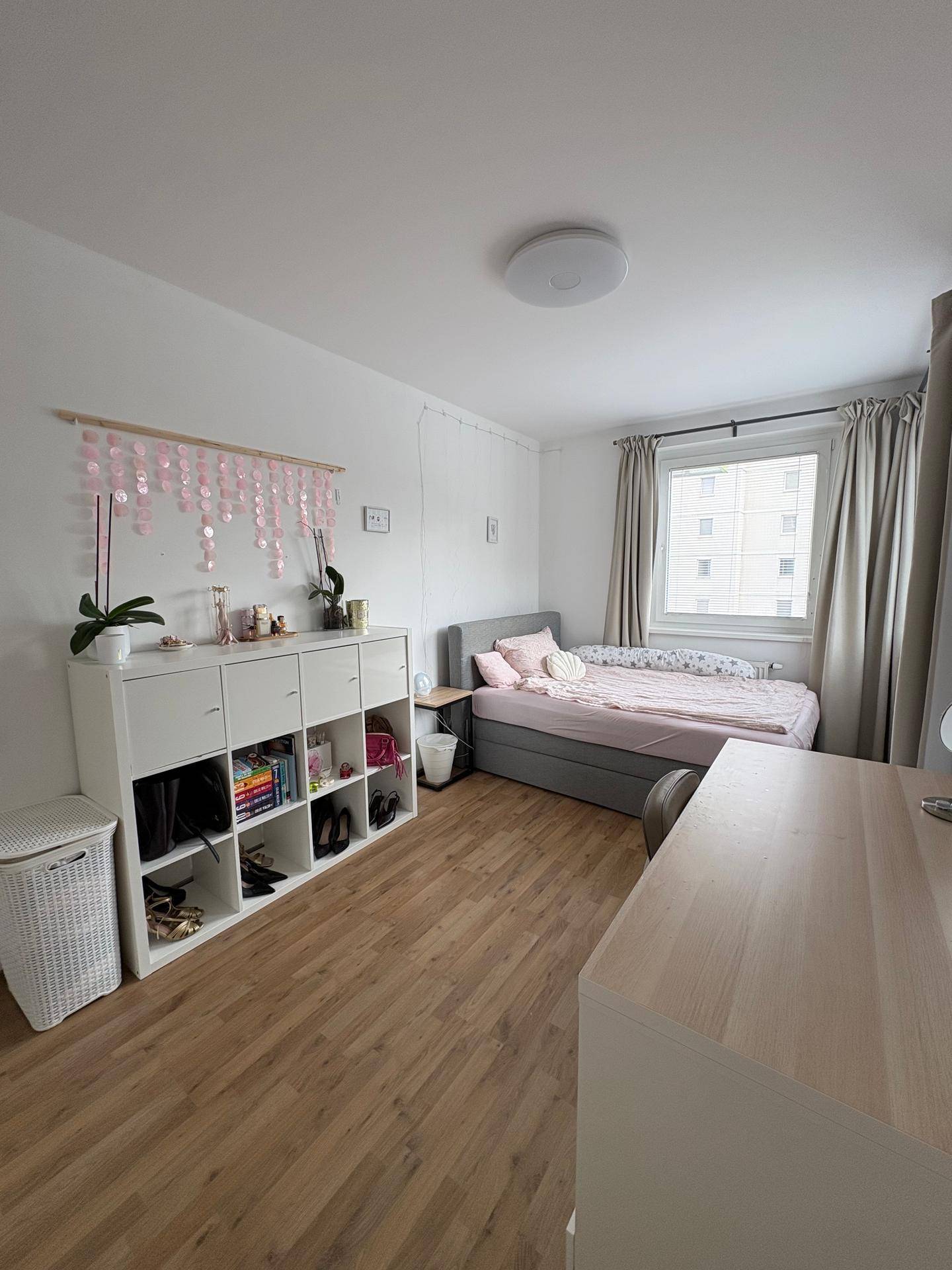 Helles Schlafzimmer mit Einzelbett, Schreibtisch und weißem Regal für Stauraum.