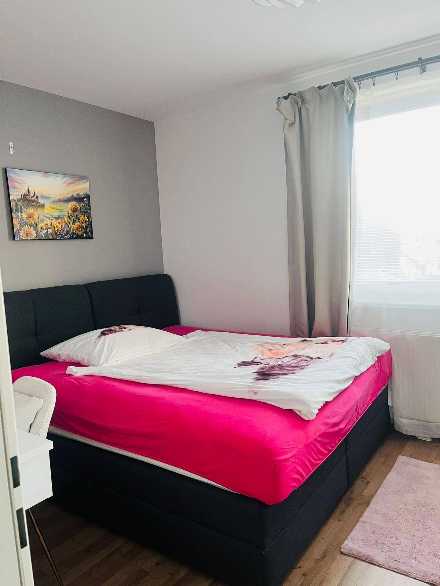 Schlafzimmer mit Doppelbett, rosa Bettwäsche und einer Akzentwand in Grau.