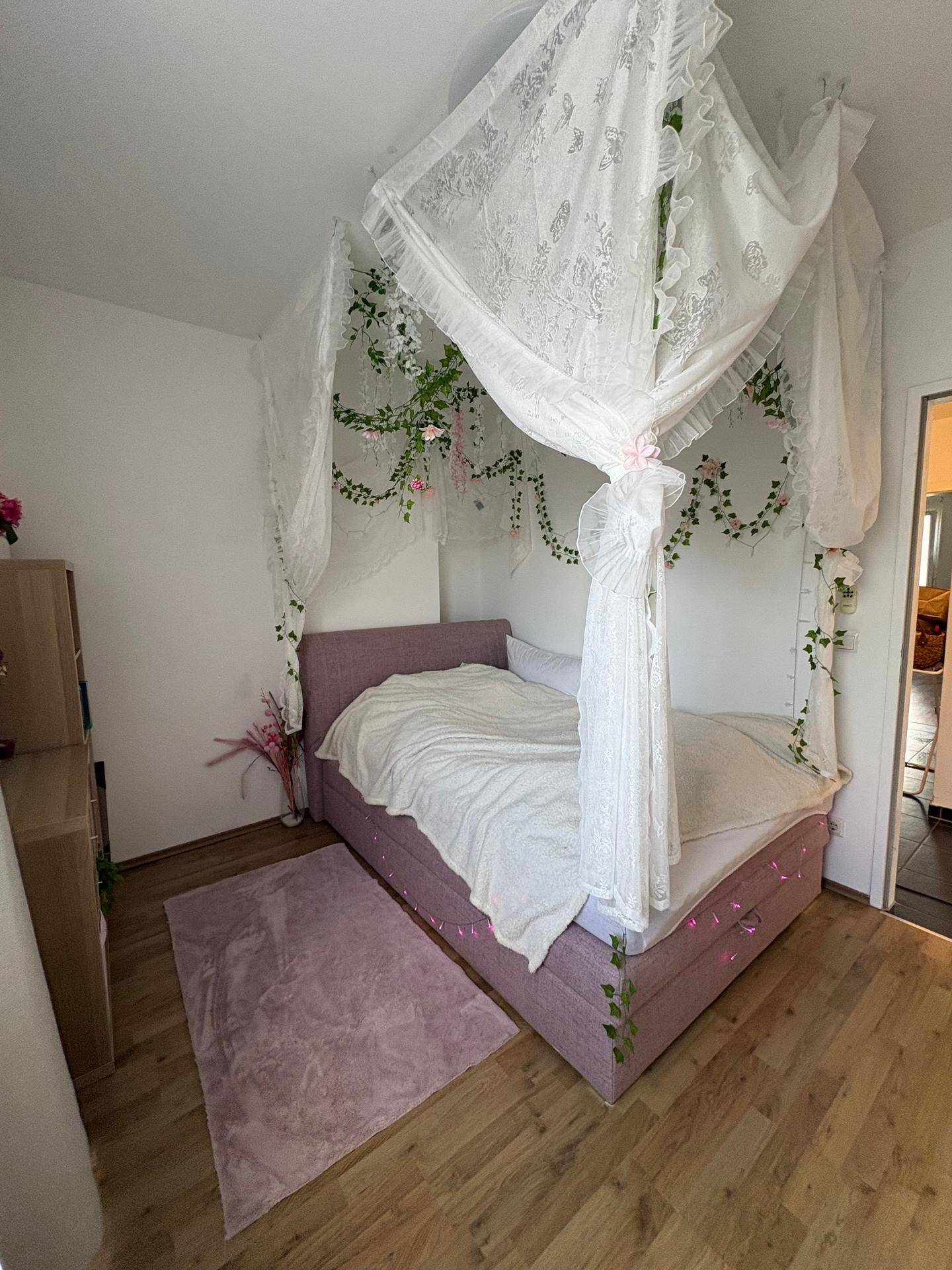 Mädchenhaftes Schlafzimmer mit Himmelbett, floraler Dekoration und hellem Holzboden.