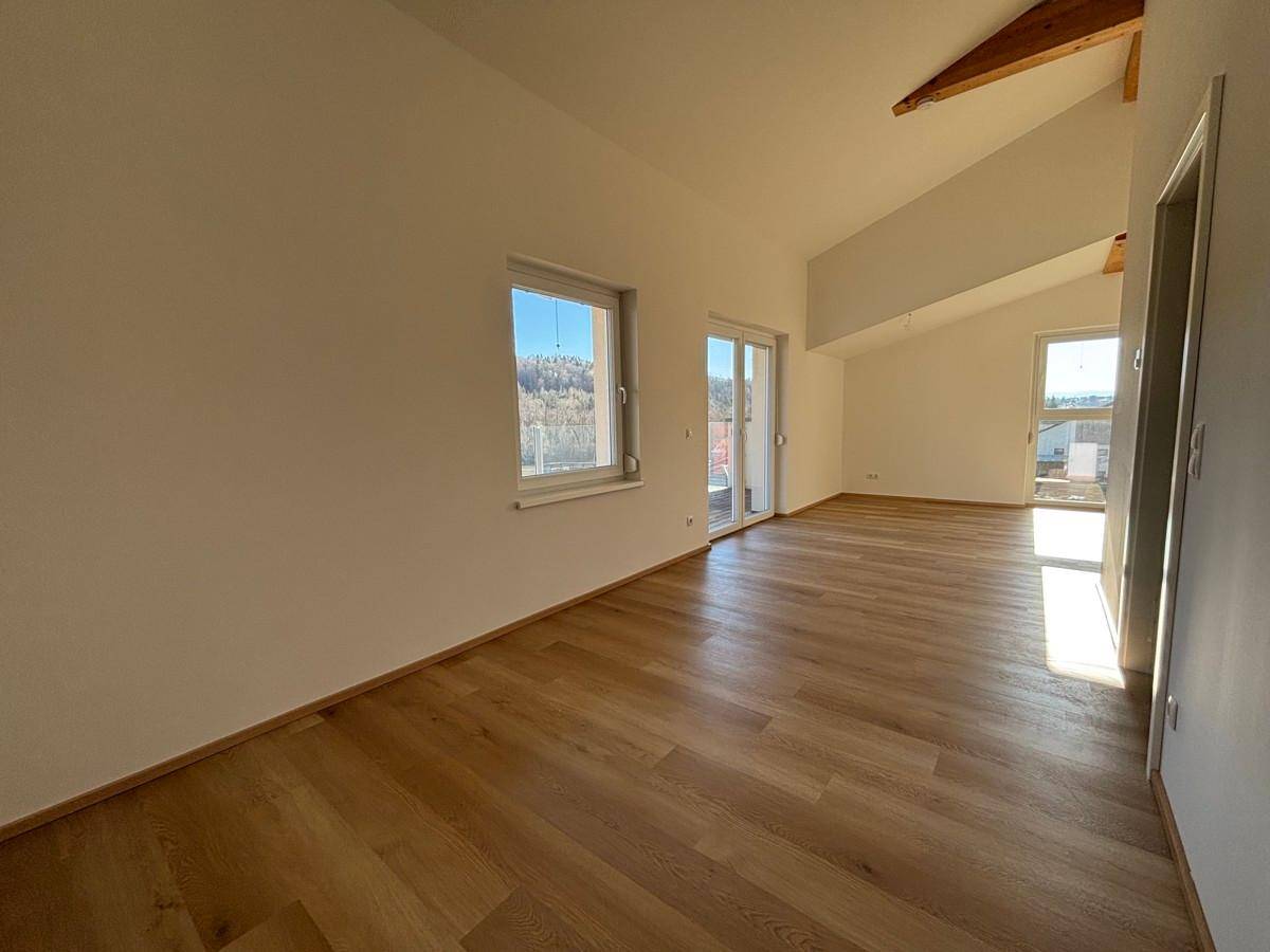 Heller Wohnraum im Dachgeschoss mit Holzbalken, Parkettboden und Zugang zur Terrasse.