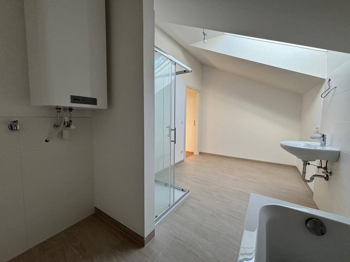 Helles Badezimmer mit Dusche, Waschbecken und schräger Decke im Dachgeschoss.