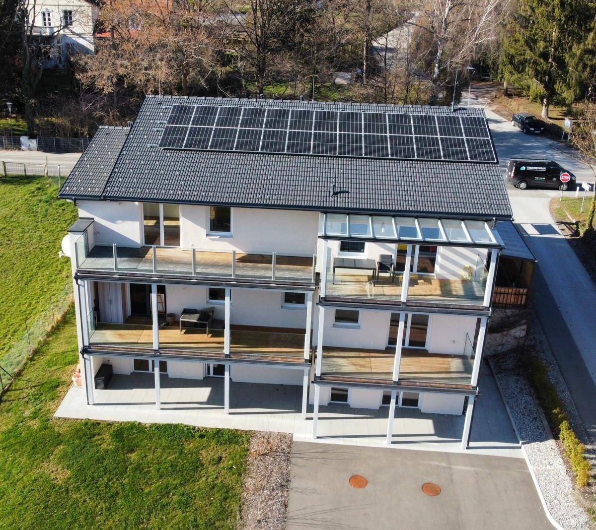 Rückansicht des Gebäudes mit mehreren Balkonen, Glasgeländern und Photovoltaikanlage auf dem Dach.