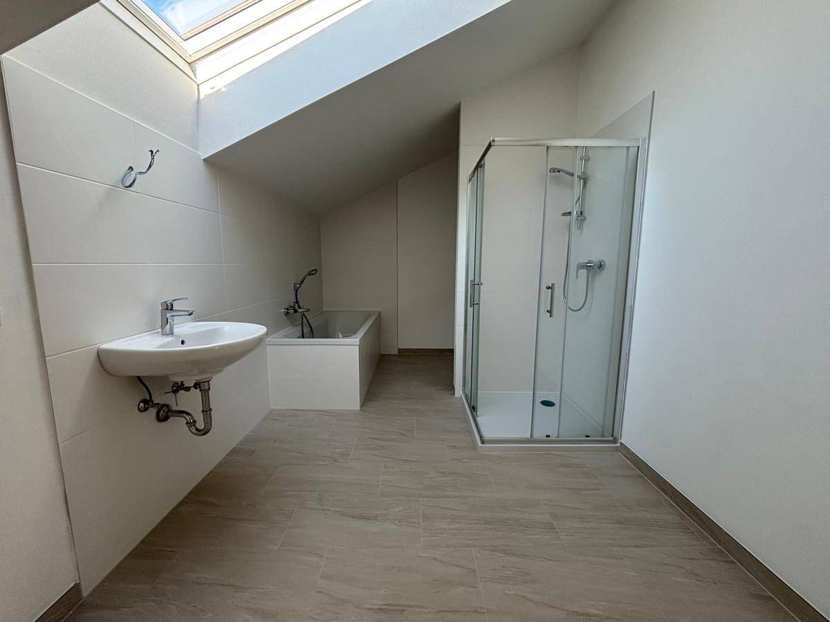 Modernes Badezimmer im Dachgeschoss mit Badewanne, Dusche und Dachfenster für Tageslicht.