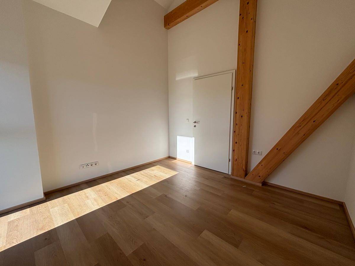 Helles Schlafzimmer im Dachgeschoss mit Holzbalken, Parkettboden und viel Tageslicht.