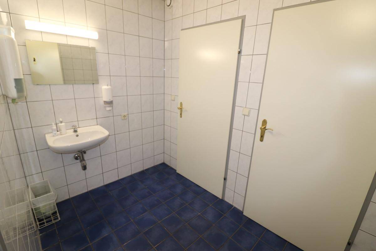 Toilettenraum mit Waschbecken, Spiegel und blauen Fliesen auf dem Boden.