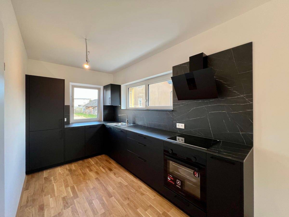 Moderne schwarze Einbauküche mit Induktionskochfeld, Backofen und Fenster für Tageslicht.
