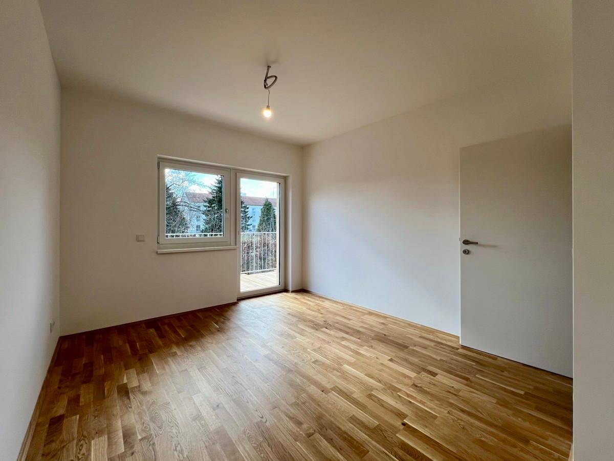 Helles Schlafzimmer mit Parkettboden und Zugang zu einem französischen Balkon mit Blick ins Grüne.