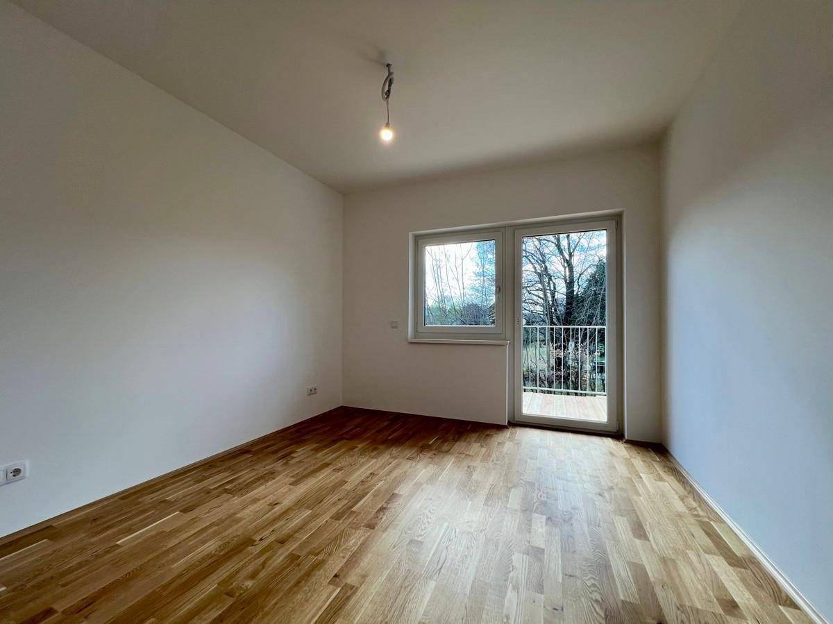 Geräumiges Schlafzimmer mit Holzboden und großen Fenstern, die den Zugang zum französischen Balkon ermöglichen.