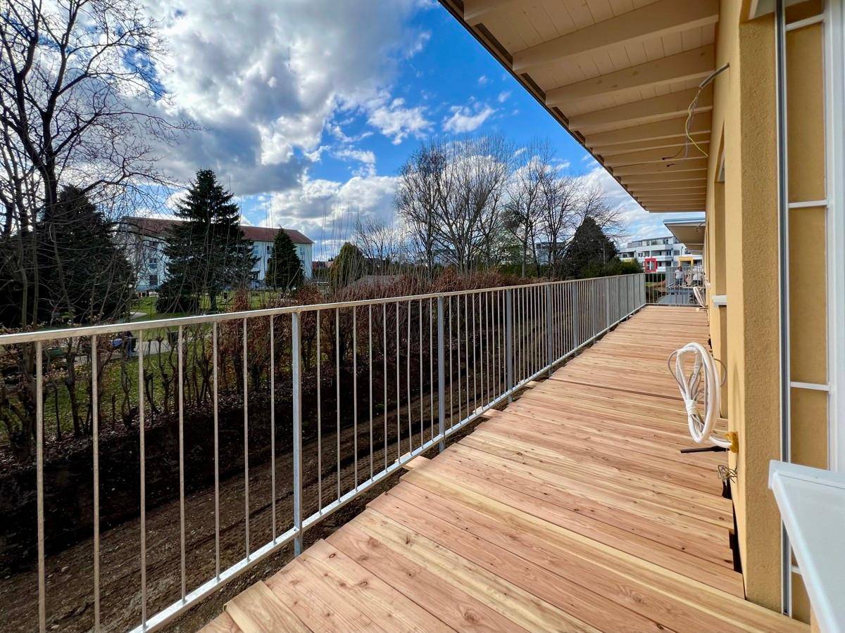 Langer Balkon mit Holzbelag und modernem Geländer, ideal für Entspannung im Freien mit Weitblick.