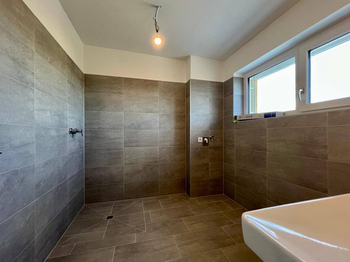 Geräumiges Badezimmer mit begehbarer Dusche, Fliesenboden und einem Fenster für helles Tageslicht.