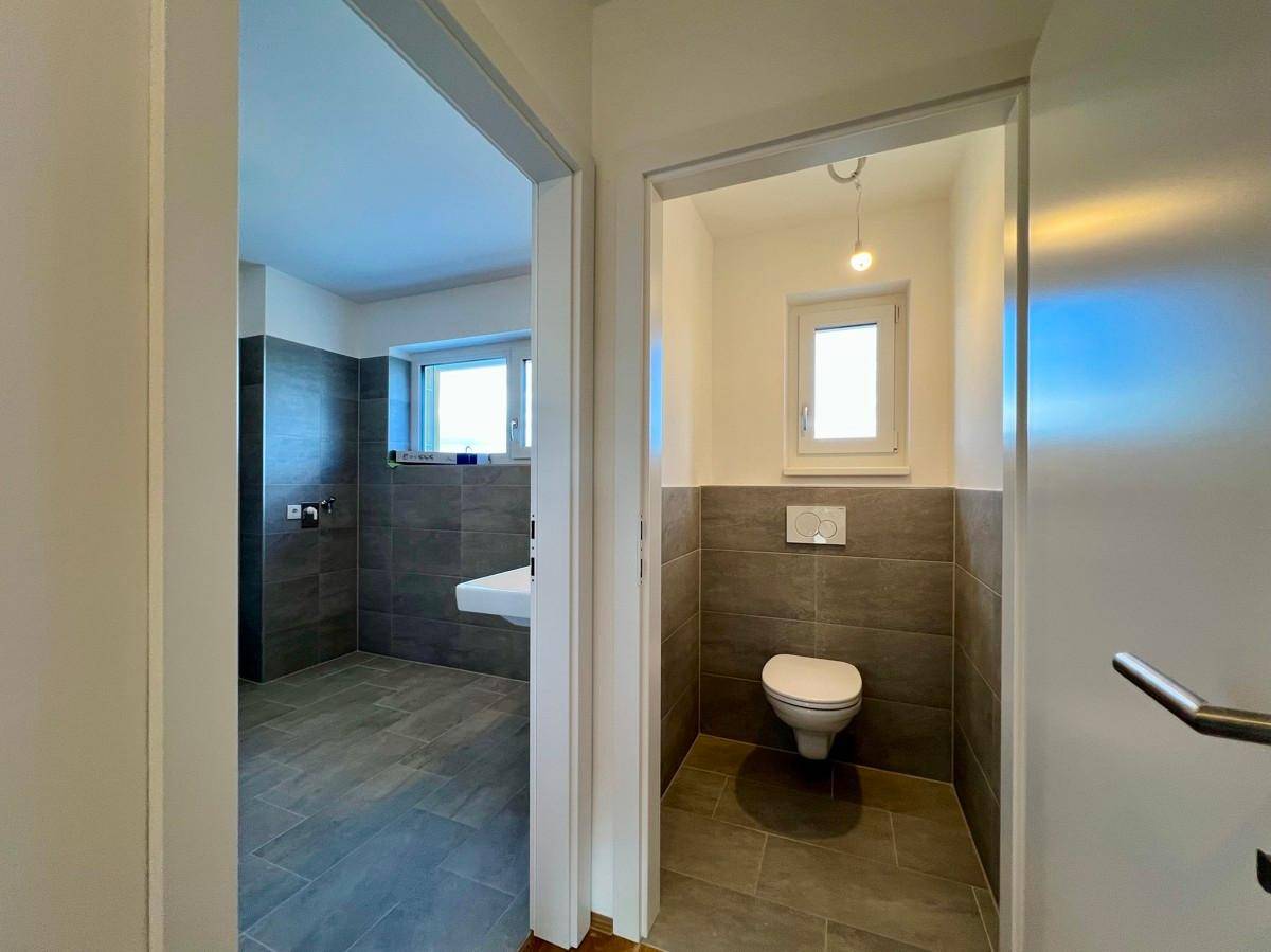 Badezimmer mit Doppelwaschbecken und separatem Gäste-WC mit wandhängender Toilette und Fenster.