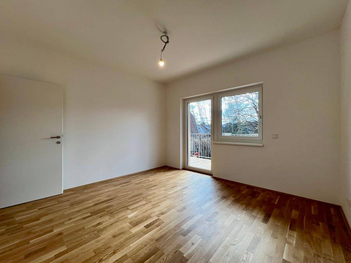 Lichtdurchflutetes Schlafzimmer mit Parkett und einem französischen Balkon, der eine angenehme Aussicht bietet.