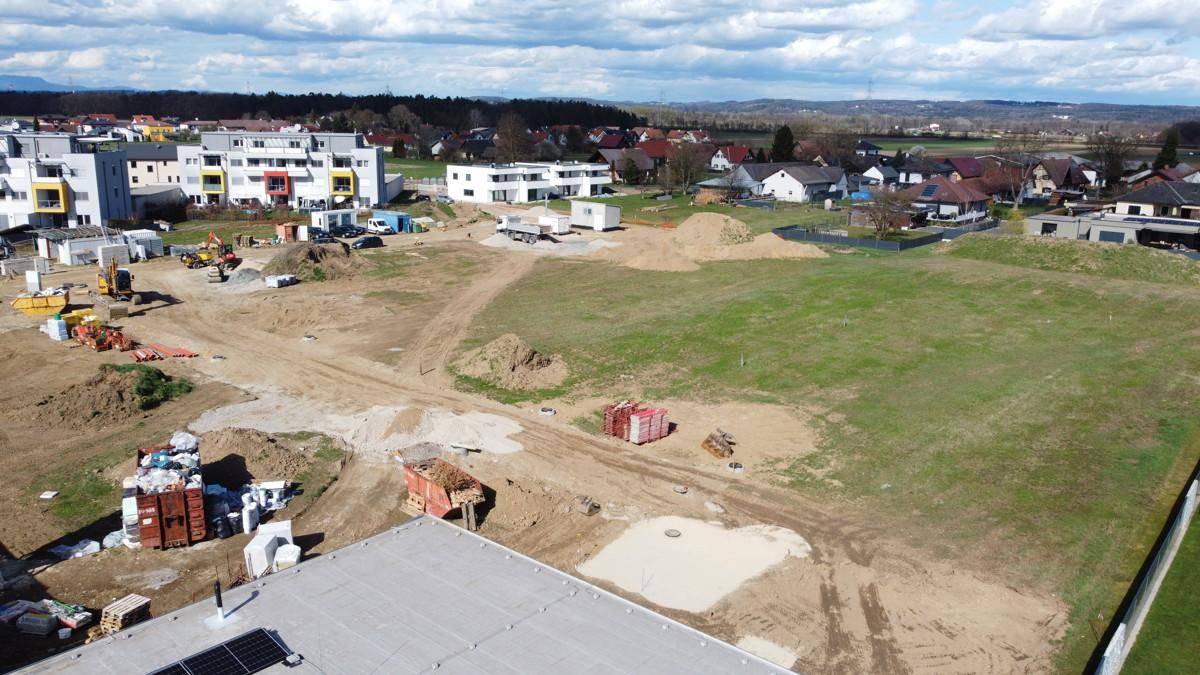 Weitläufige Drohnenaufnahme einer Baustelle mit viel unbebautem Land und weiteren Gebäuden im Hintergrund.