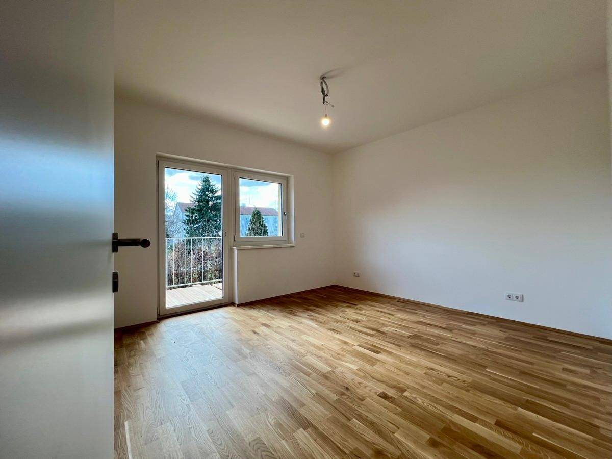 Modernes Schlafzimmer mit Holzboden und einem französischen Balkon, der für frische Luft sorgt.
