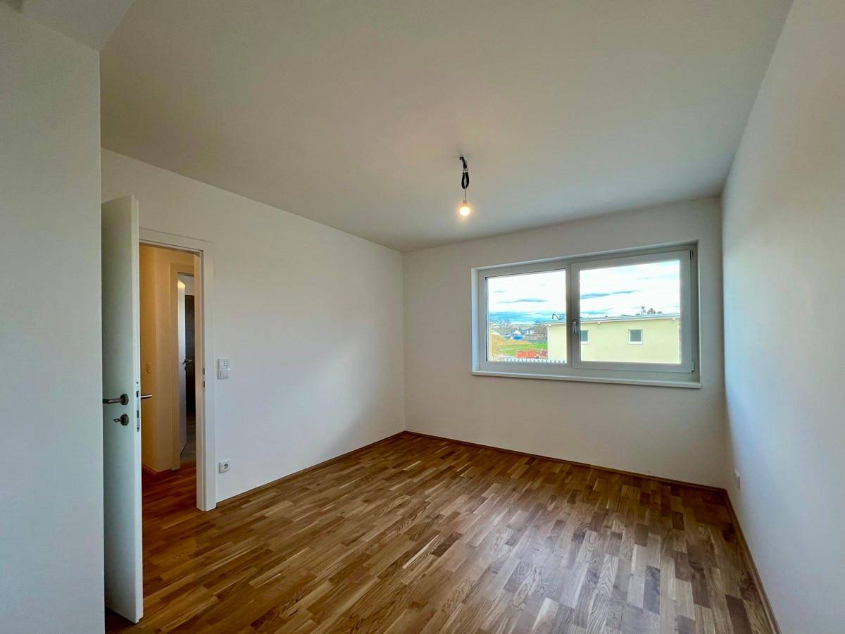 Helles Schlafzimmer mit Parkettboden und einem großen Fenster, das einen weiten Blick ermöglicht.