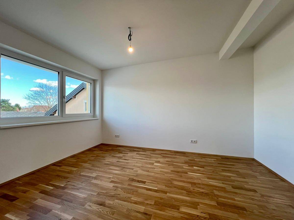 Gemütliches Schlafzimmer mit Parkettboden, Fenster und einer leichten Dachschräge, die Charakter verleiht.