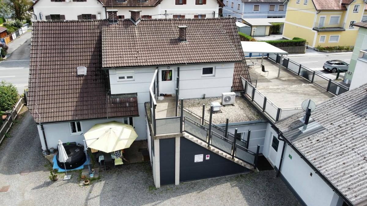 Luftaufnahme der Gebäuderückseite mit großer Terrasse, Sonnenschirm und Außentreppe.