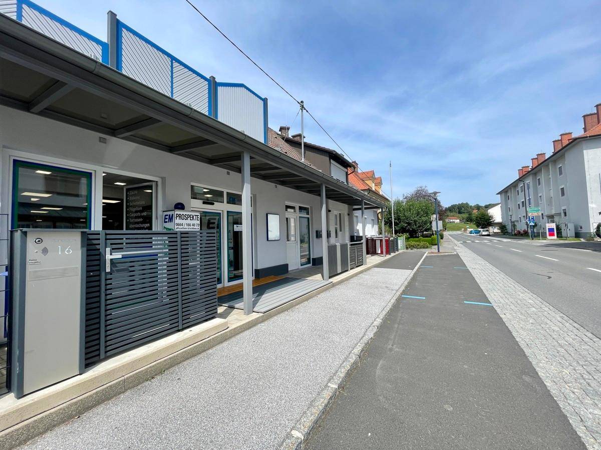 Gebäudefassade an einer Hauptstraße mit überdachtem Eingangsbereich und Werbeschildern.