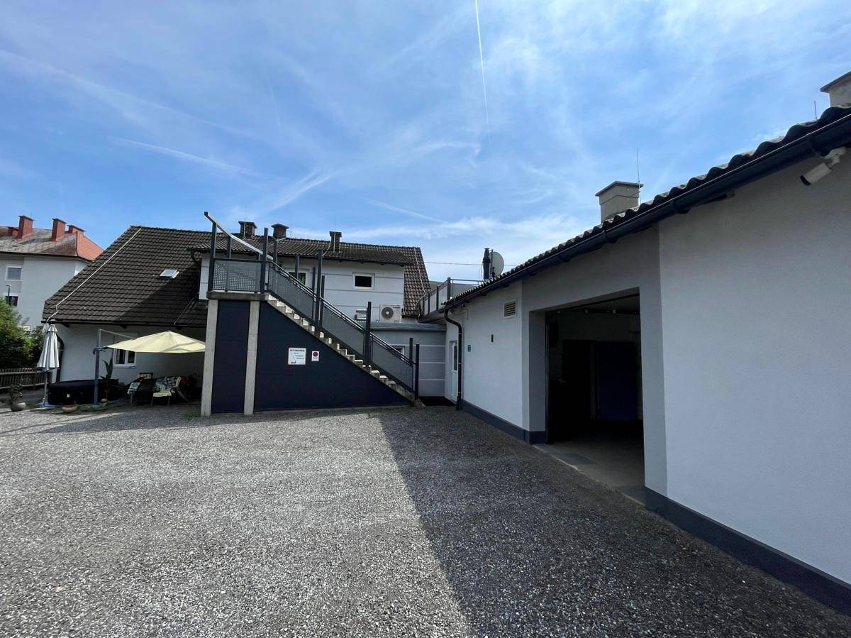 Rückseite des Gebäudes mit Außentreppe, Parkplatz und einem Sonnenschirm im Hofbereich.