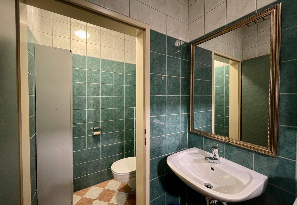 Gefliestes WC mit Waschbecken, Spiegel und separaten Kabinen in grünen Farbtönen.