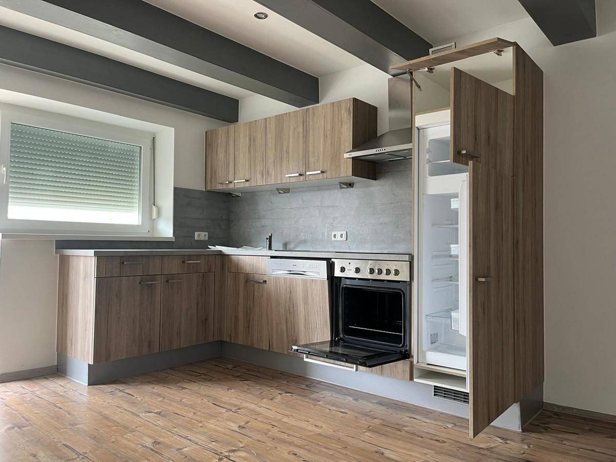 Moderne Einbauküche mit Holzfronten, integrierten Geräten und offenem Kühlschrank.