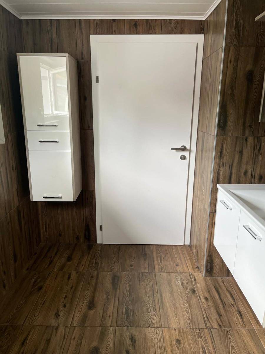 Modernes Badezimmer mit Holzeffektfliesen und weißem Hängeschrank.