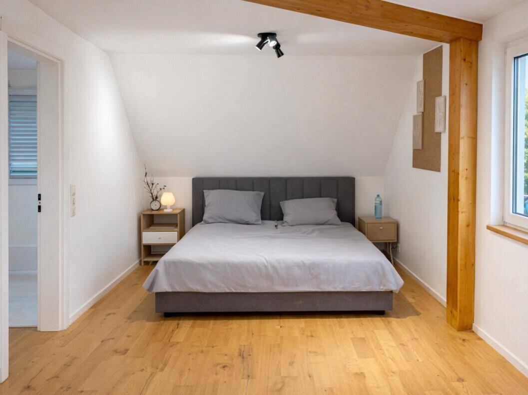 Helles Schlafzimmer im Dachgeschoss mit Holzboden und sichtbarem Holzbalken.