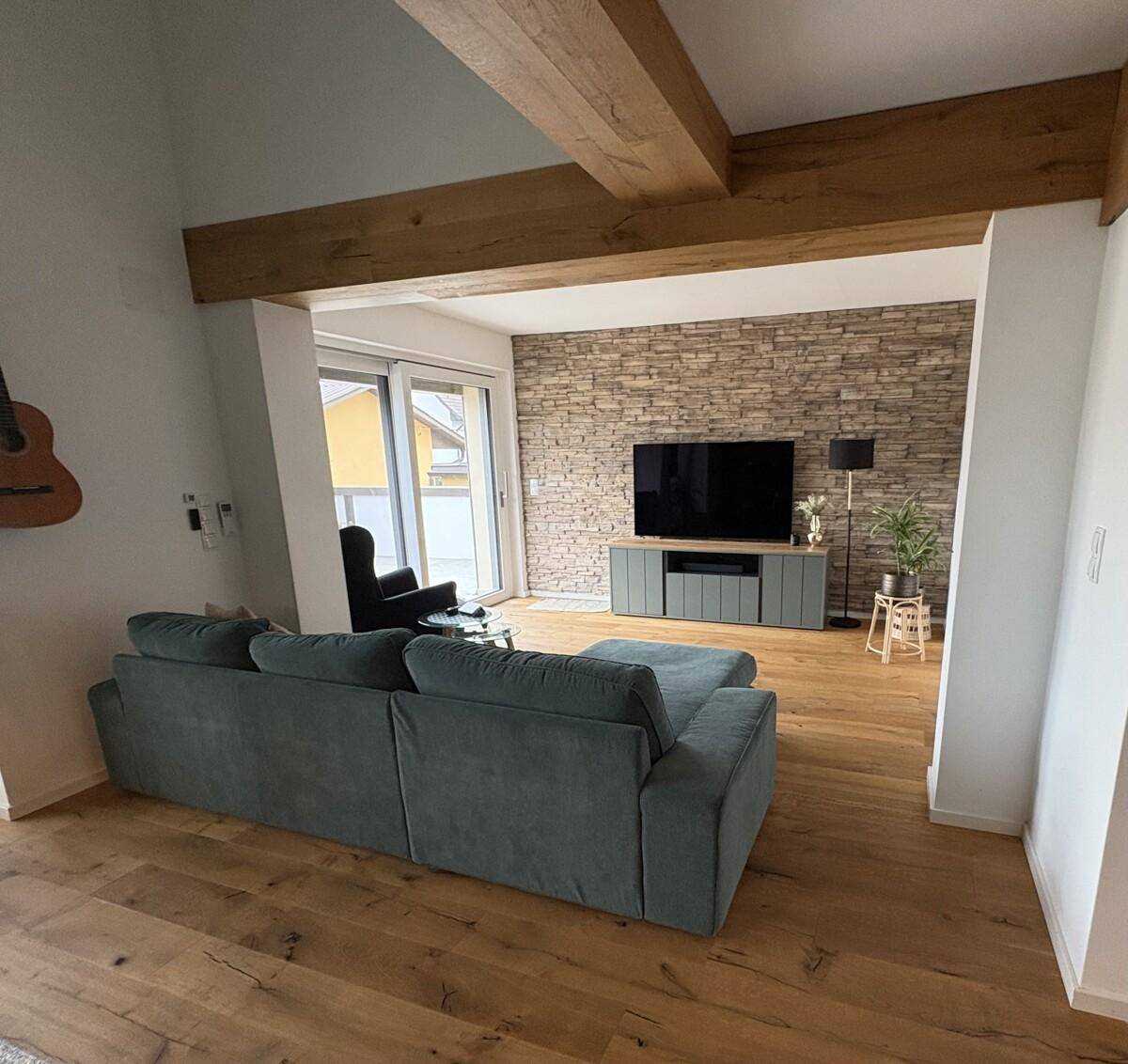 Gemütliches Wohnzimmer mit Holzbalken, Steinwand und Zugang zur Terrasse.
